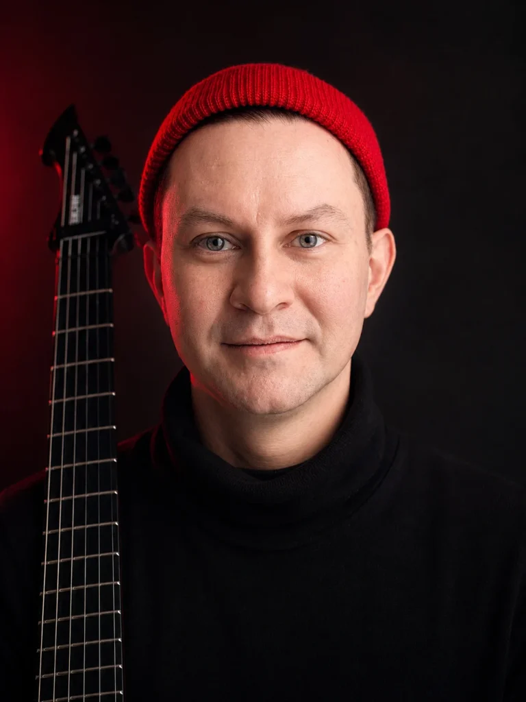 Portrait of Andrew Nitsievsky holding an electric guitar and wearing a red beanie